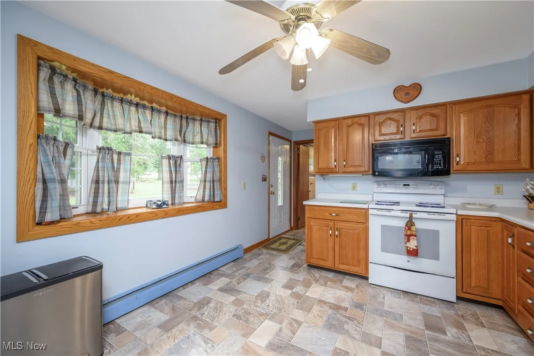 Kitchen featuring black microwave, white range with electric stovetop, baseboard heating, light countertops, and brown cabinets