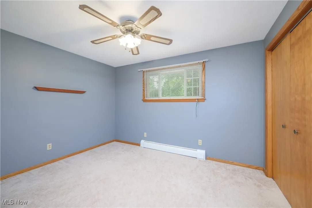 Unfurnished bedroom featuring baseboard heating, a closet, carpet flooring, and ceiling fan