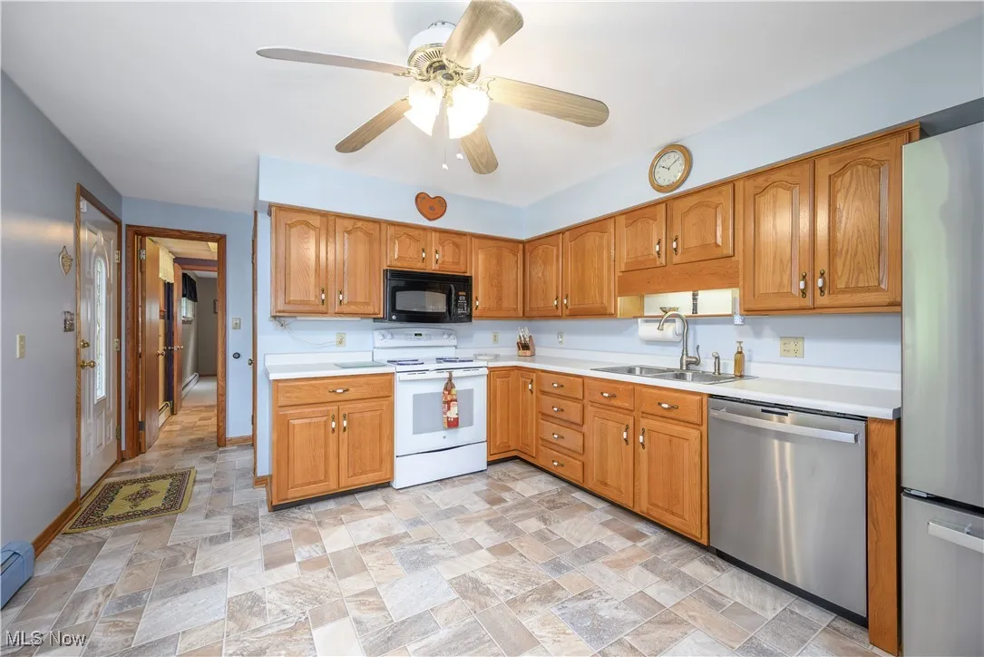 Kitchen featuring appliances with stainless steel finishes, stone finish flooring, light countertops, ceiling fan, and brown cabinets