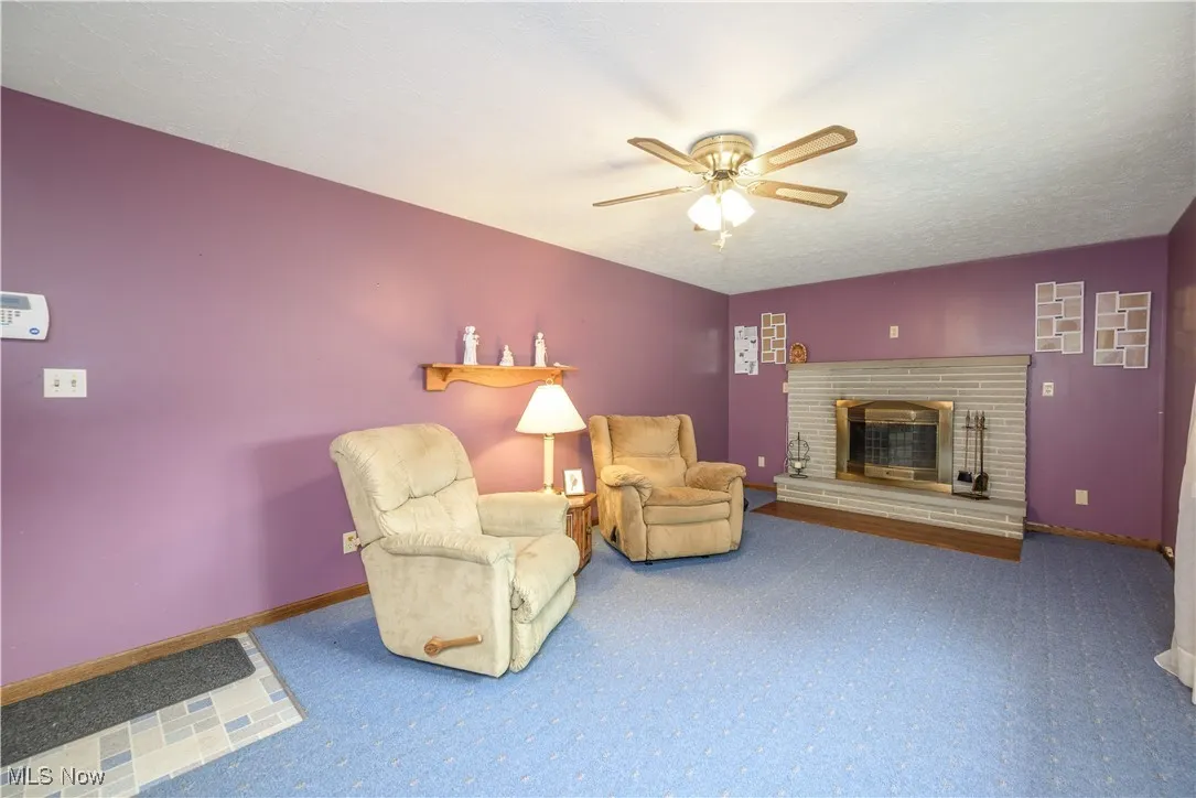 Living room with carpet flooring, a ceiling fan, and a fireplace