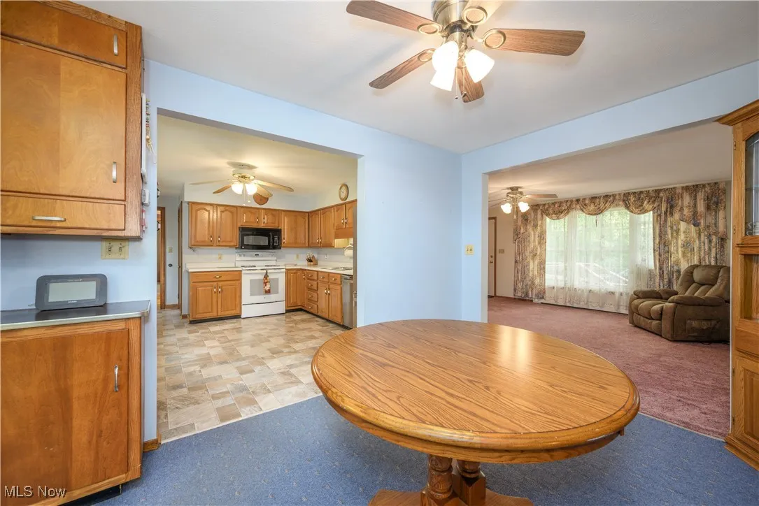 Kitchen with electric stove, black microwave, a ceiling fan, and brown cabinets