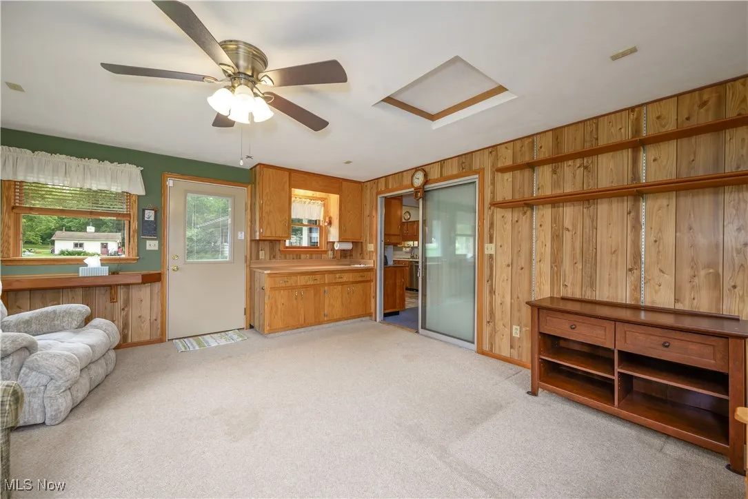 Living room with a ceiling fan, light colored carpet, and wooden walls