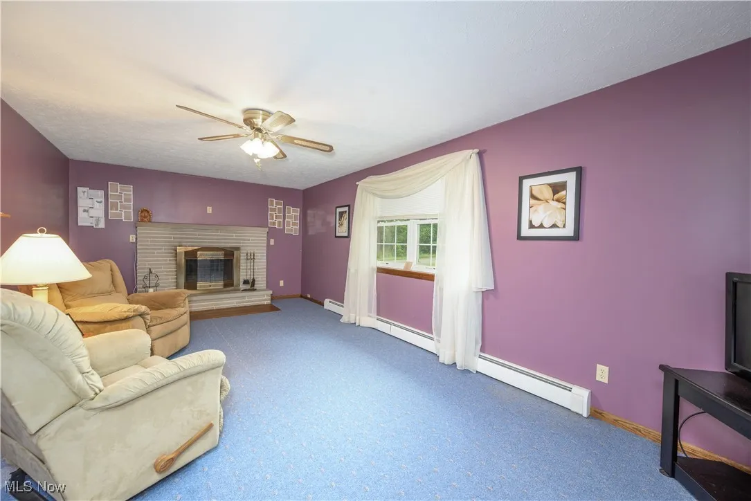 Carpeted living area with baseboard heating, a ceiling fan, and a brick fireplace