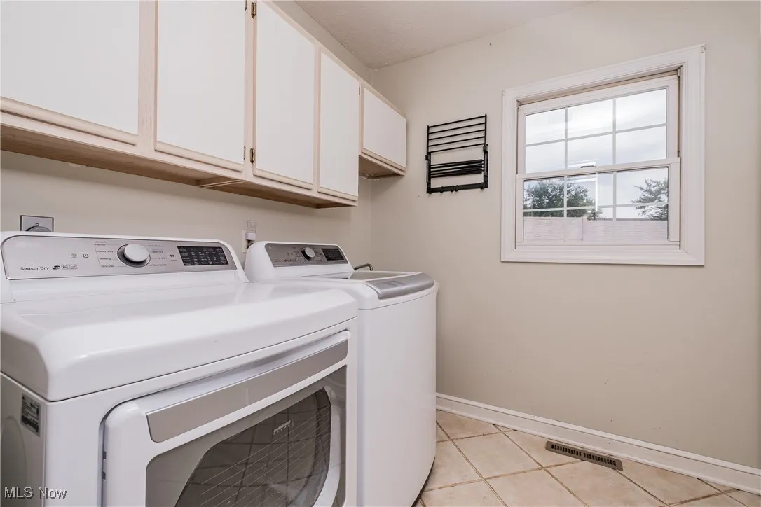 Laundry area featuring washing machine and clothes dryer, cabinet space, and light tile patterned floors