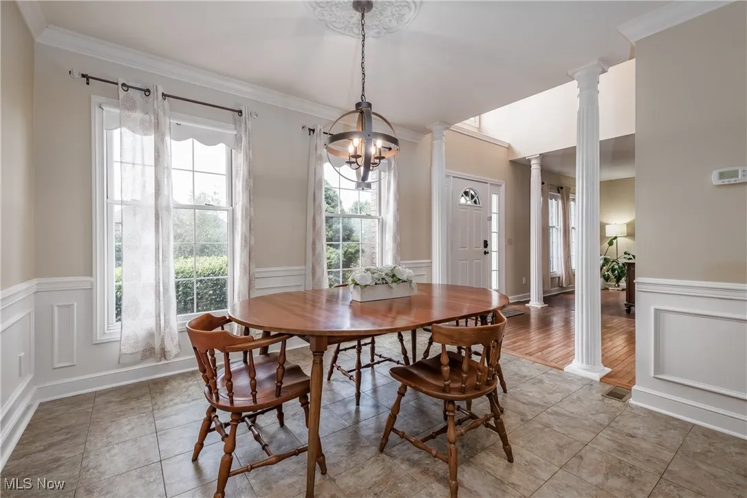 Dining space with decorative columns, a wainscoted wall, a decorative wall, a chandelier, and crown molding