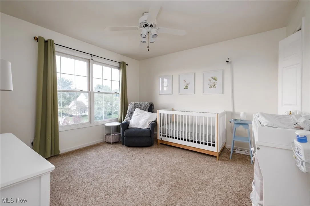 Carpeted bedroom featuring a crib and ceiling fan