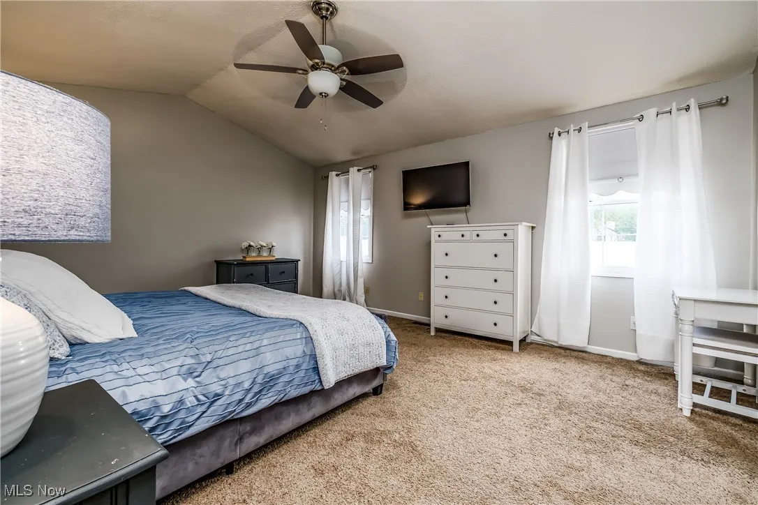 Carpeted bedroom with multiple windows, vaulted ceiling, and a ceiling fan