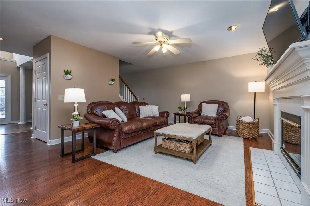 Living area featuring a fireplace with flush hearth, ceiling fan, wood finished floors, decorative columns, and recessed lighting