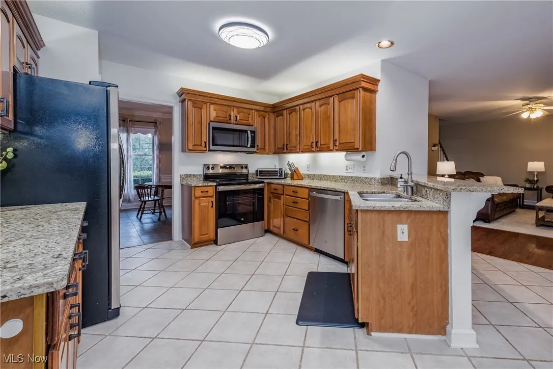 Kitchen featuring stainless steel appliances, a peninsula, light tile patterned flooring, brown cabinetry, and a kitchen bar