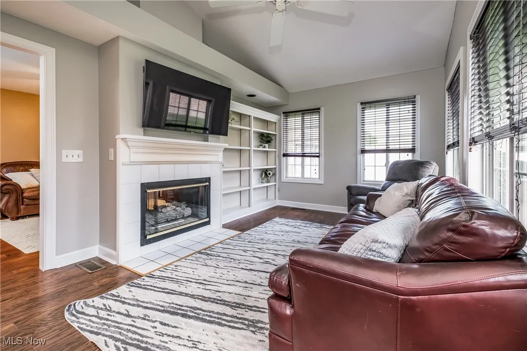 Living area with a tiled fireplace, lofted ceiling, dark wood-style flooring, and ceiling fan