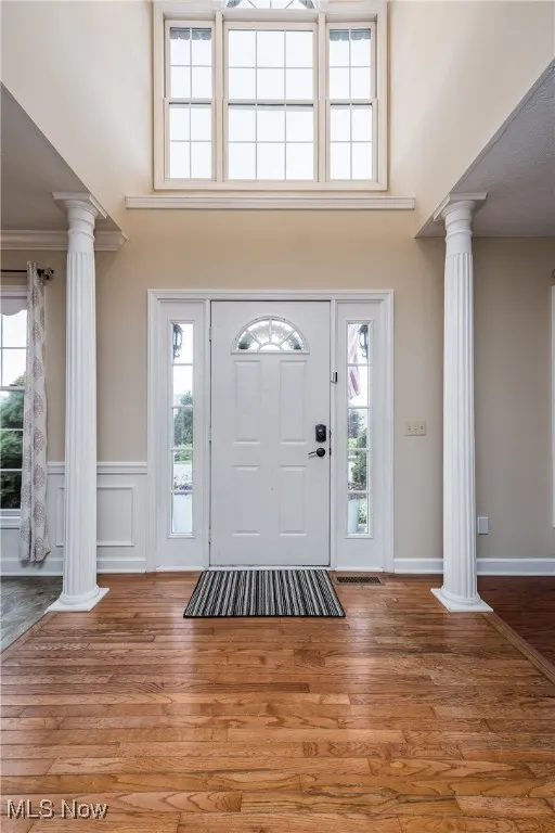 Entryway with ornate columns, healthy amount of natural light, a high ceiling, and a wainscoted wall