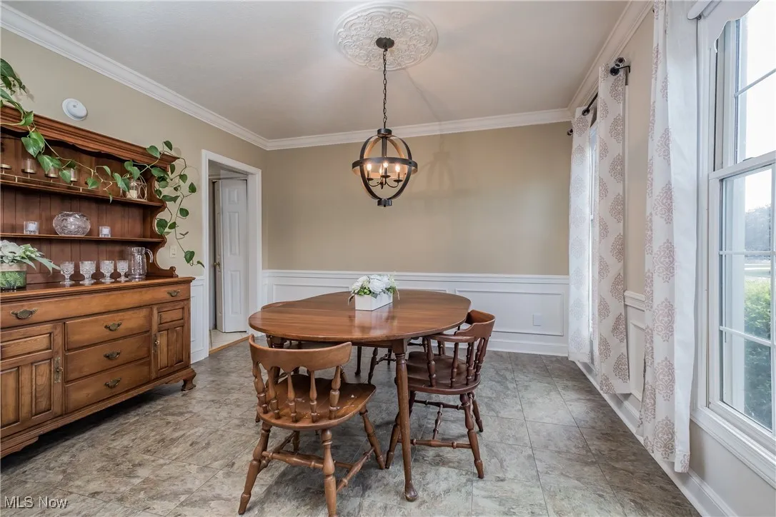 Dining room with a chandelier, healthy amount of natural light, ornamental molding, and a wainscoted wall