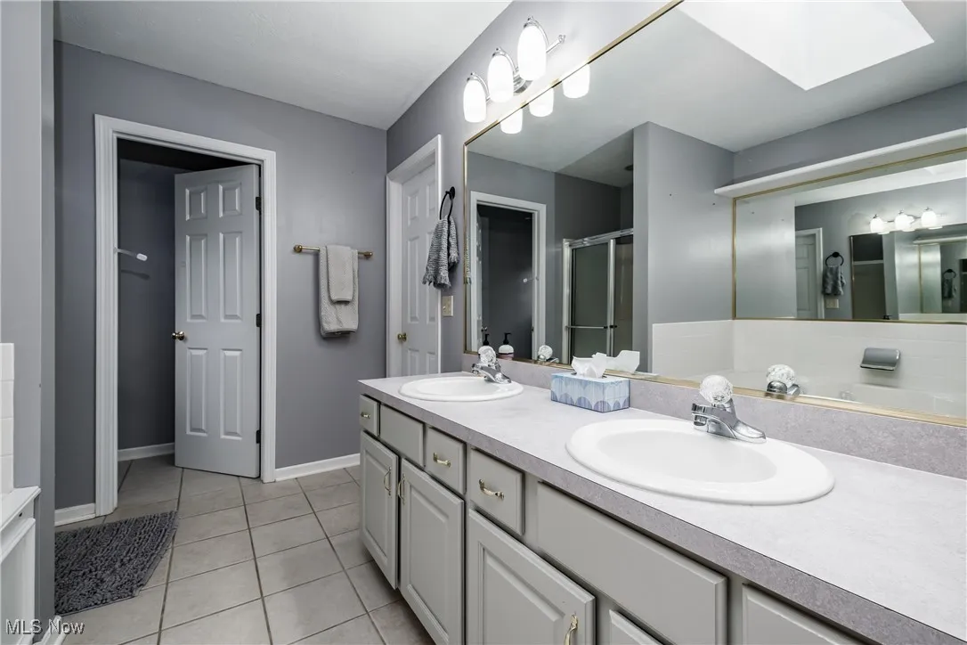 Bathroom featuring double vanity, tile patterned flooring, a stall shower, and a skylight