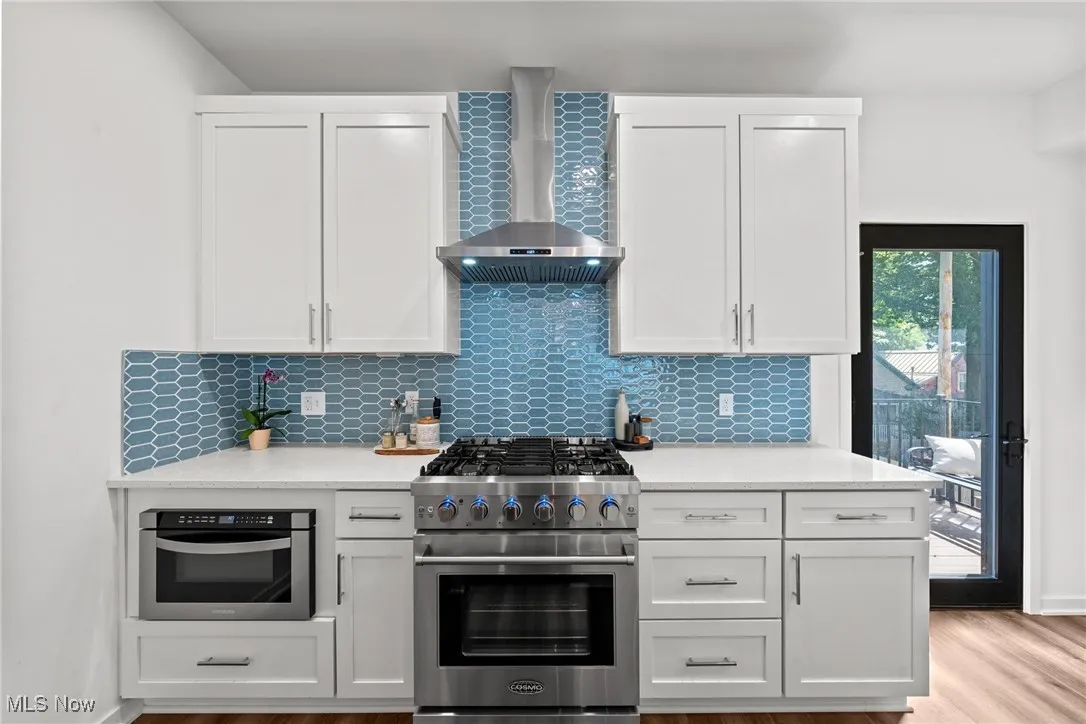Kitchen featuring stainless steel appliances, wall chimney range hood, light countertops, and decorative backsplash
