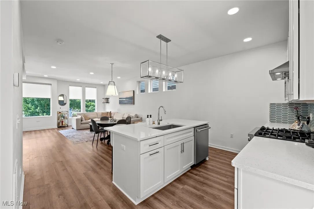 Kitchen with dishwasher, wall chimney range hood, white cabinets, open floor plan, and dark wood-type flooring