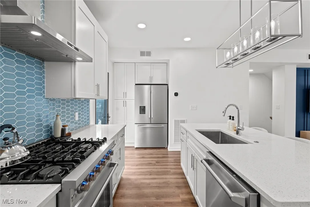 Kitchen with stainless steel appliances, extractor fan, recessed lighting, backsplash, and white cabinets