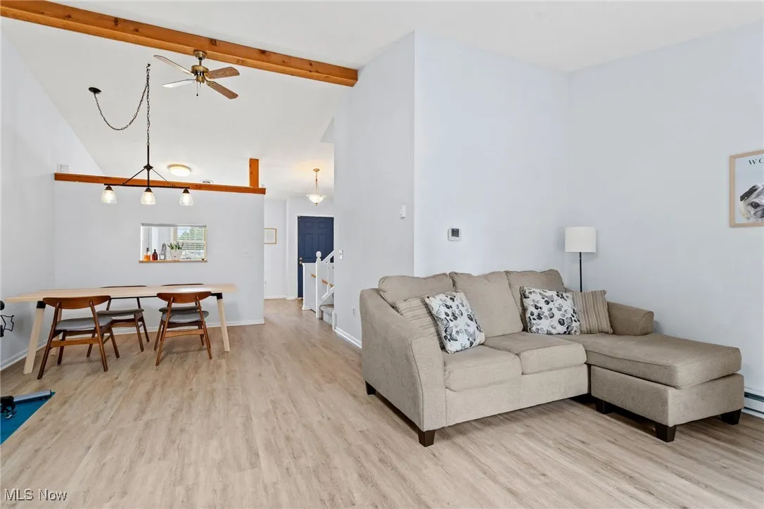 Living room with light wood finished floors, ceiling fan, beamed ceiling, and high vaulted ceiling