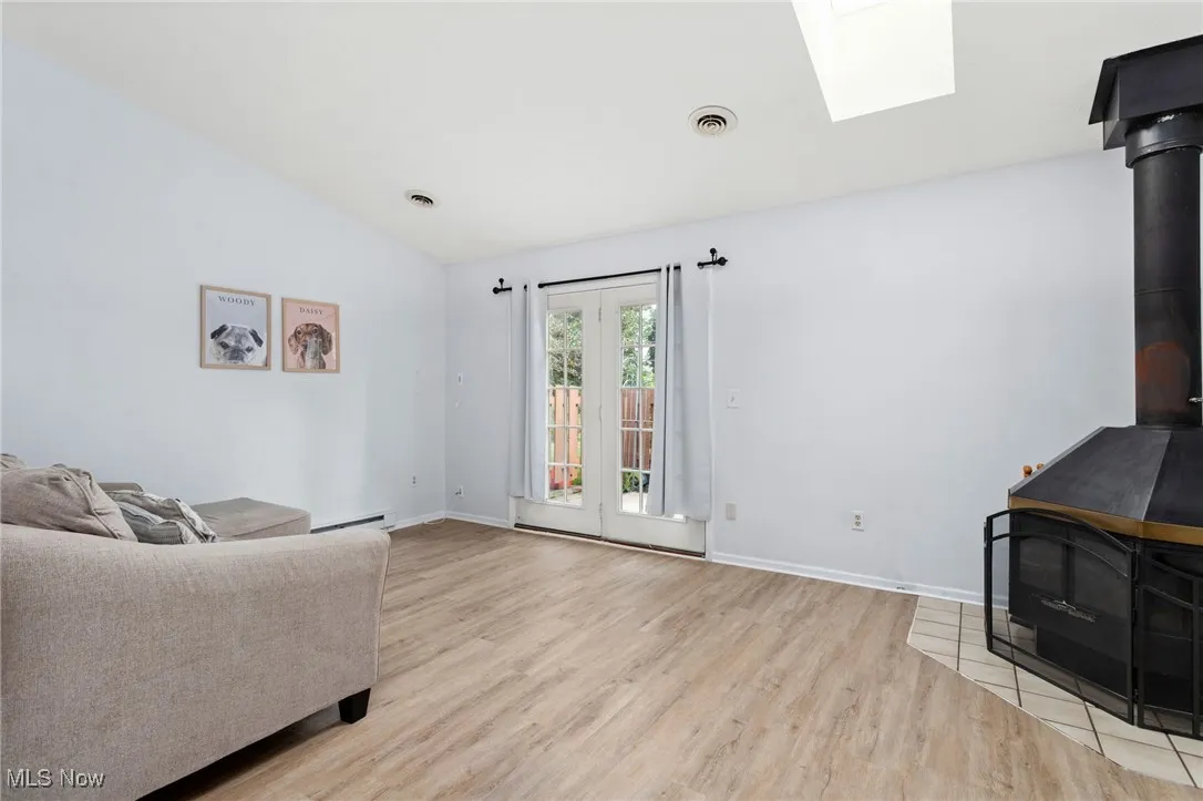 Living area with vaulted ceiling, light wood-style flooring, a skylight, a baseboard radiator, and a wood stove