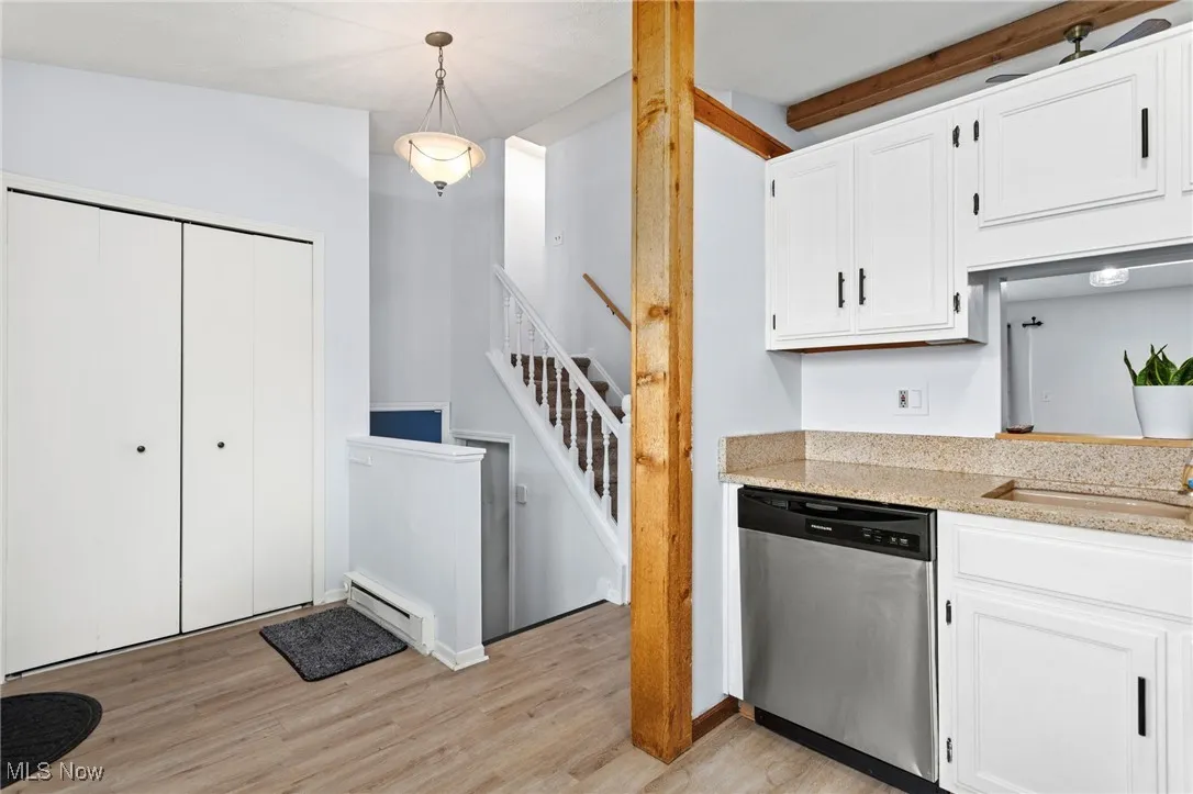 Kitchen featuring stainless steel dishwasher, baseboard heating, light wood-style flooring, white cabinets, and beamed ceiling