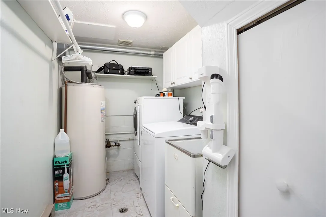 Laundry area featuring gas water heater, washer and clothes dryer, cabinet space, and light marble finish flooring