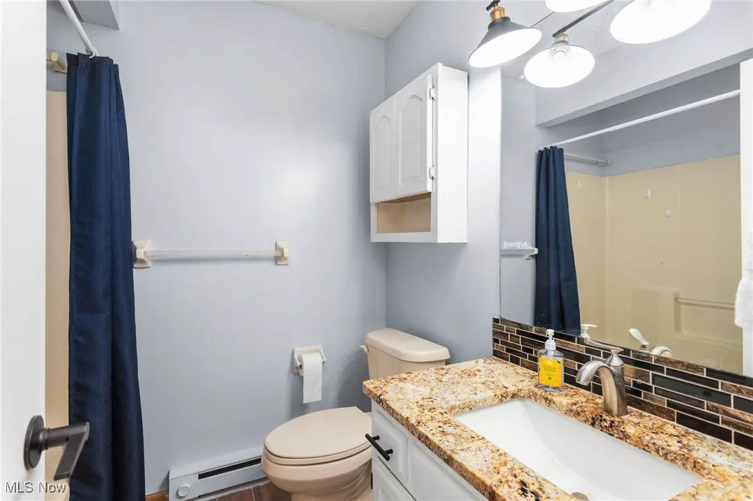 Full bathroom with a baseboard heating unit, vanity, curtained shower, and tasteful backsplash
