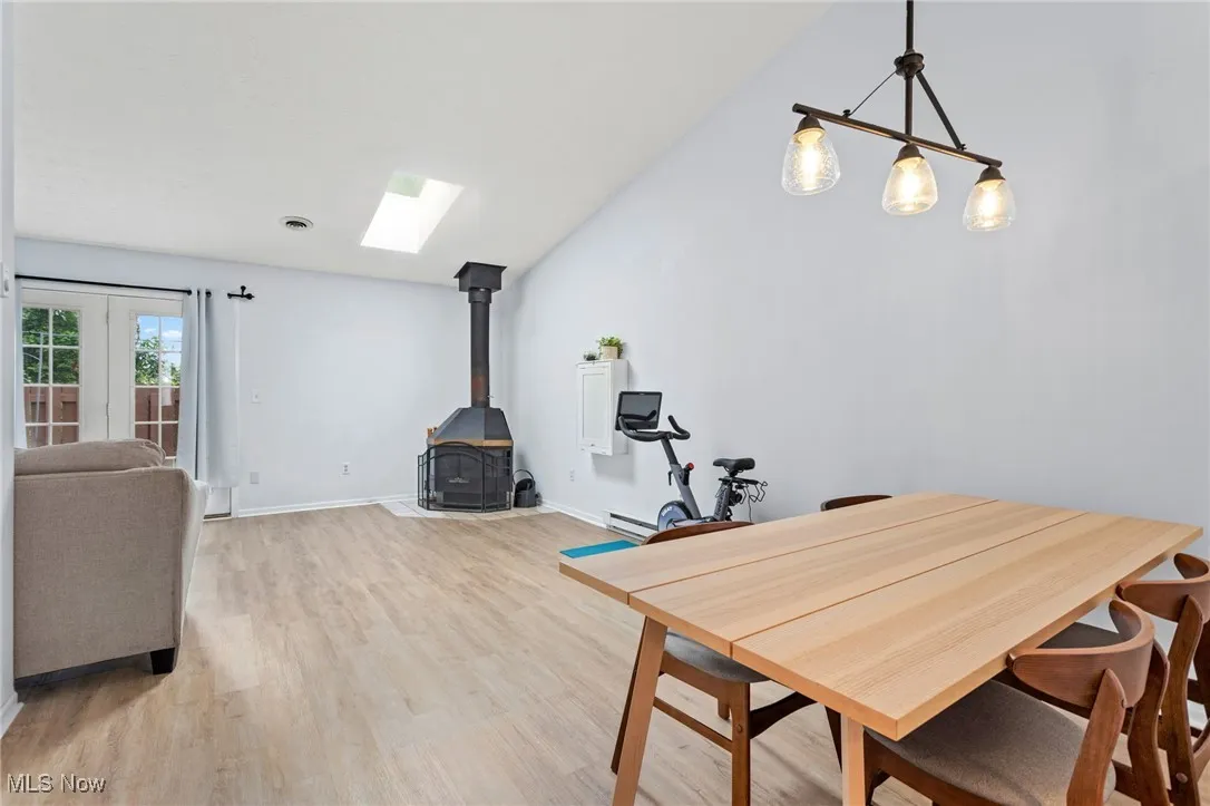 Dining space with a wood stove, a baseboard heating unit, light wood-type flooring, a skylight, and french doors