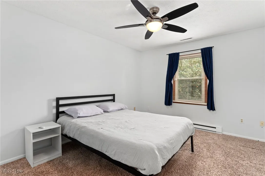 Bedroom with a baseboard heating unit, carpet flooring, and a ceiling fan