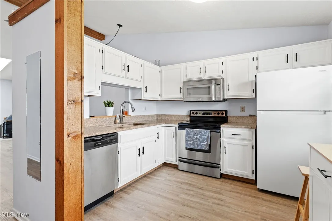 Kitchen with stainless steel appliances, lofted ceiling, white cabinets, light countertops, and light wood-style flooring