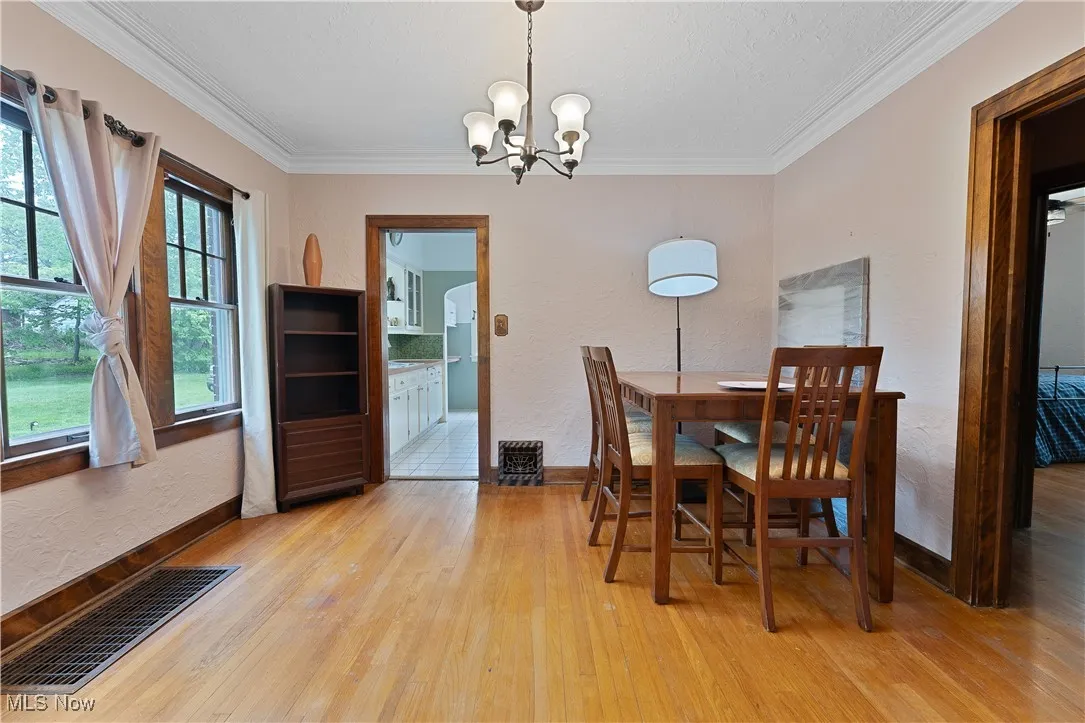 Dining area featuring light wood-style flooring, a chandelier, crown molding, and a textured wall
