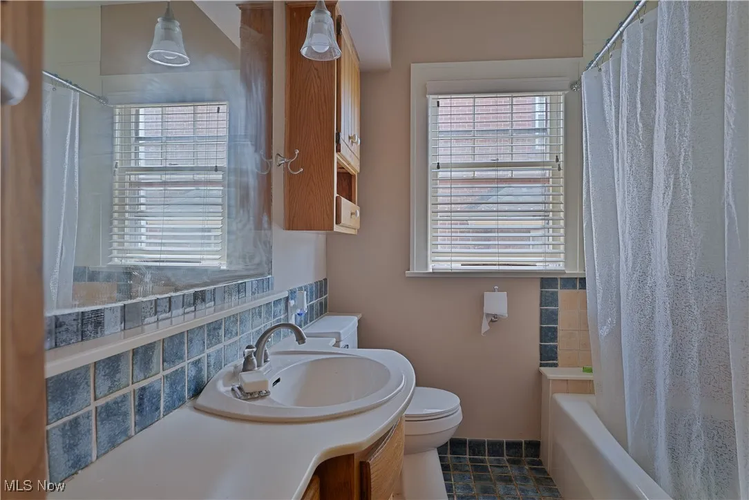 Full bath featuring vanity, healthy amount of natural light, shower / bathtub combination with curtain, and backsplash