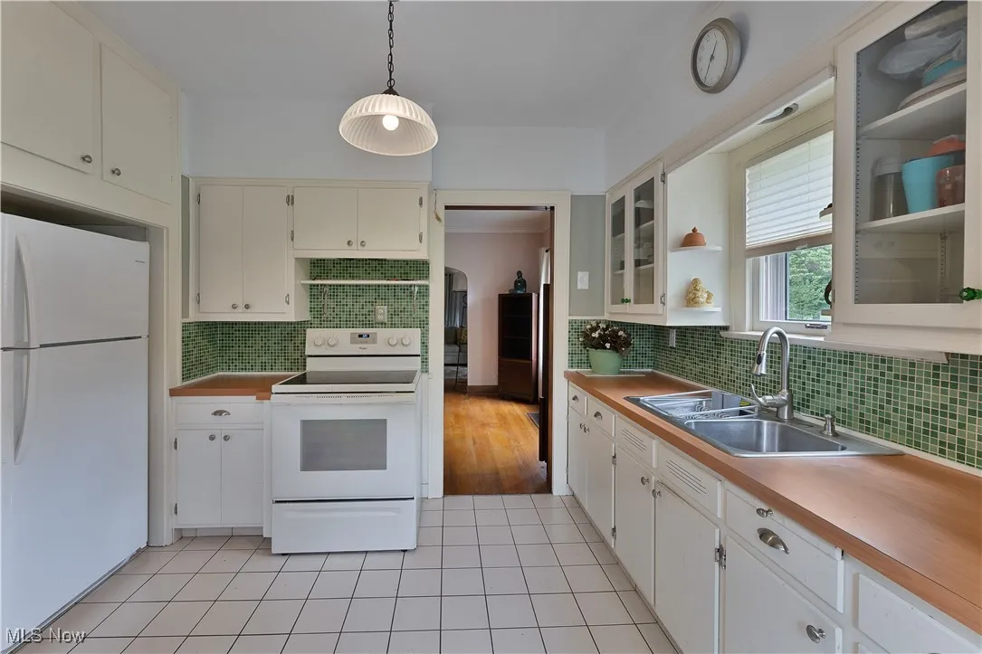 Kitchen with white appliances, tasteful backsplash, light tile patterned flooring, glass insert cabinets, and decorative light fixtures