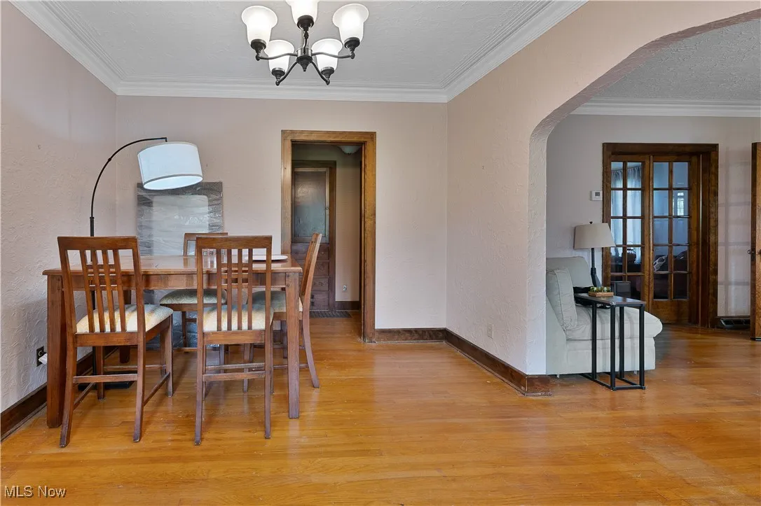 Dining area featuring arched walkways, a chandelier, light wood-style floors, ornamental molding, and a textured wall