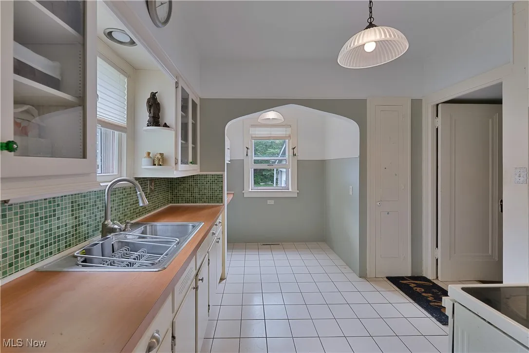 Kitchen with arched walkways, decorative backsplash, glass insert cabinets, and white cabinetry