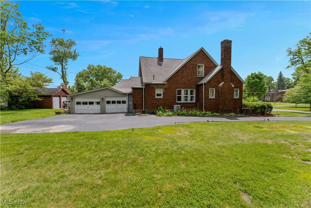 View of front facade with brick siding, a front yard, a detached garage, and a chimney