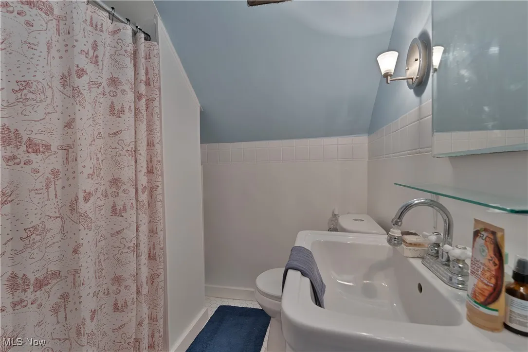 Full bathroom featuring a shower with shower curtain, vaulted ceiling, and tile patterned floors