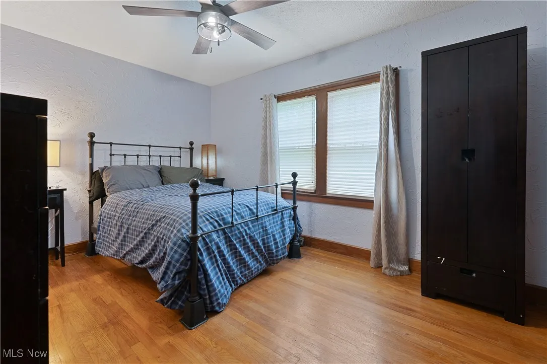 Bedroom featuring light wood-style floors, a textured wall, and ceiling fan