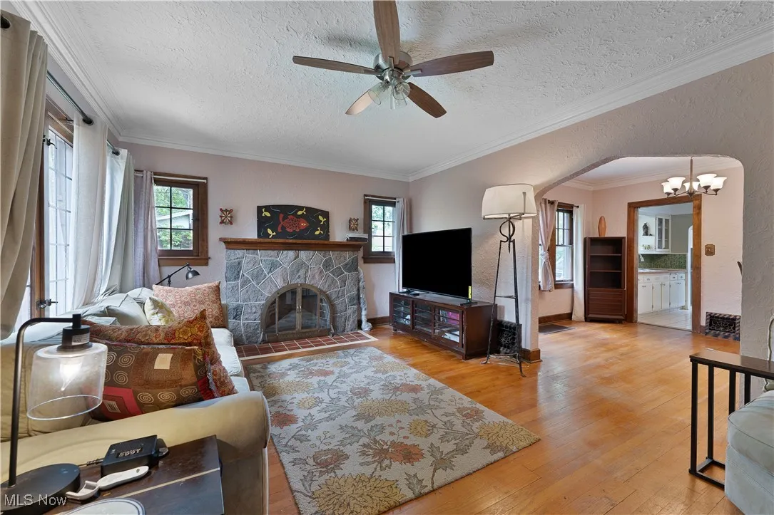 Living room featuring wood finished floors, ceiling fan, a chandelier, a textured ceiling, and a stone fireplace