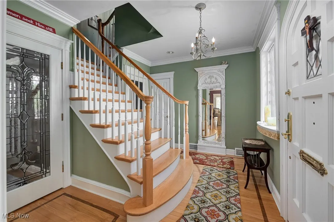 Entrance foyer with wood finished floors, stairs, a chandelier, and ornamental molding