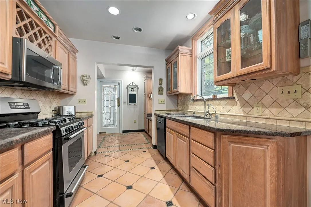 Kitchen with appliances with stainless steel finishes, glass insert cabinets, dark stone countertops, tasteful backsplash, and recessed lighting
