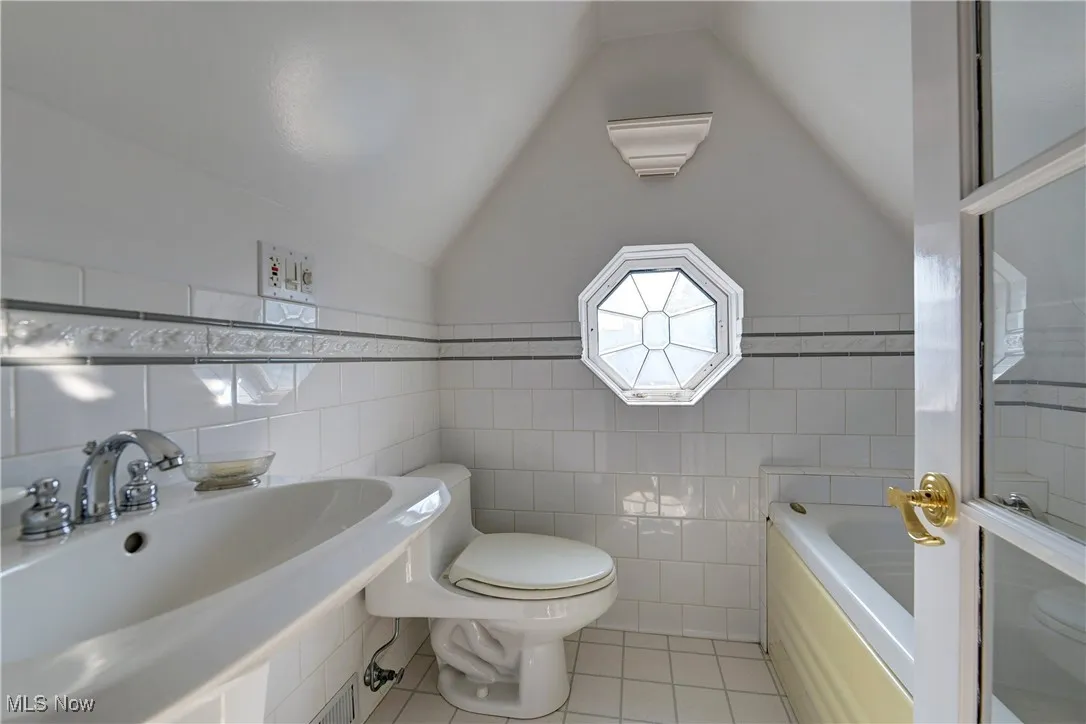 Full bathroom featuring tile walls, tile patterned flooring, vaulted ceiling, and a bath