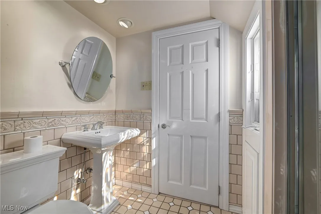 Bathroom featuring tile walls, tile patterned flooring, wainscoting, and vaulted ceiling
