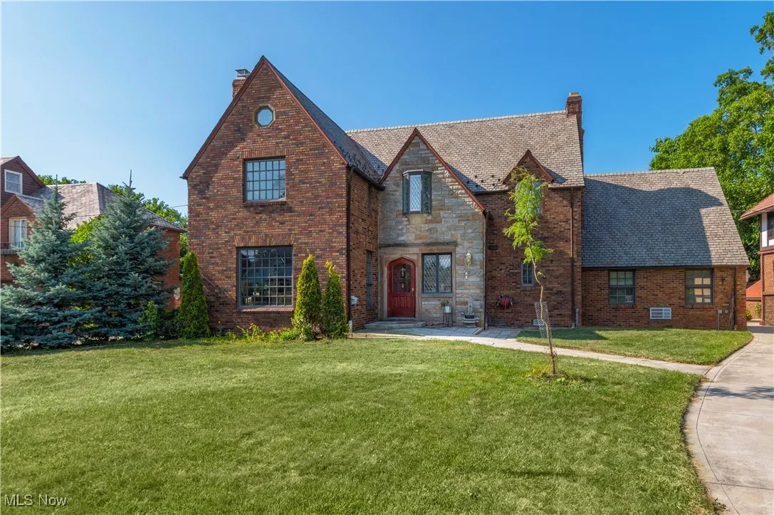 Tudor-style house featuring a chimney, a front yard, and brick siding