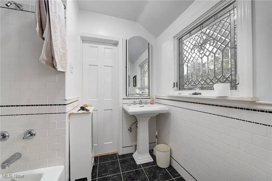 Full bath with vaulted ceiling, tile walls, tile patterned flooring, and shower / bathtub combination