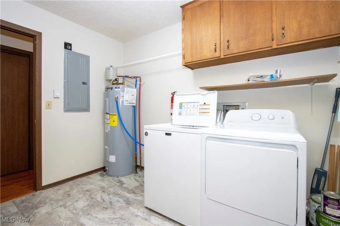 Laundry room with water heater, electric panel, washing machine and dryer, and cabinet space