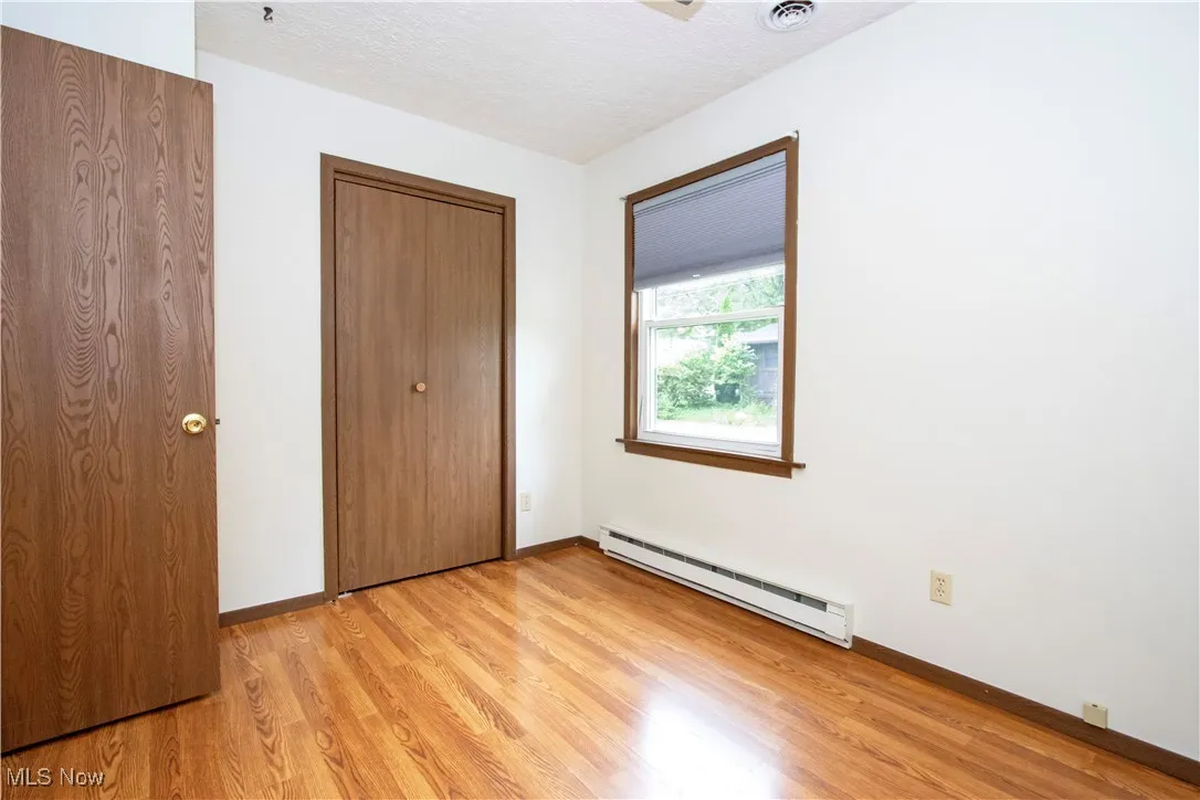 Unfurnished bedroom featuring baseboard heating, light wood-style floors, and a closet