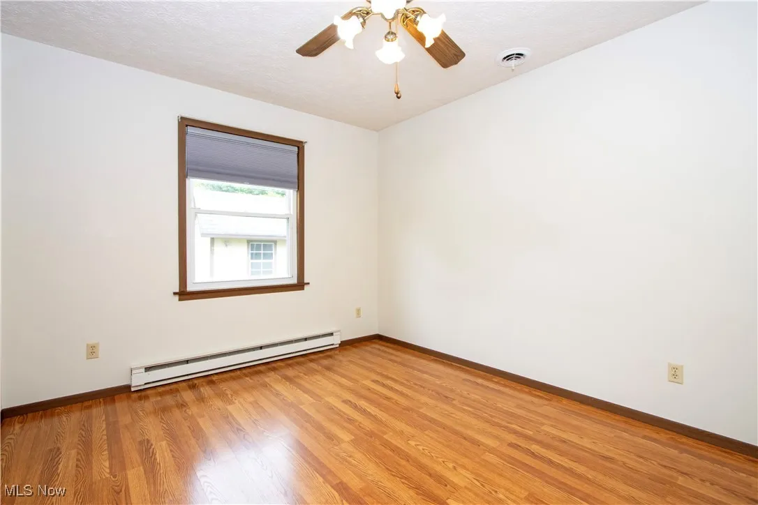 Empty room with baseboard heating, light wood-style floors, and ceiling fan