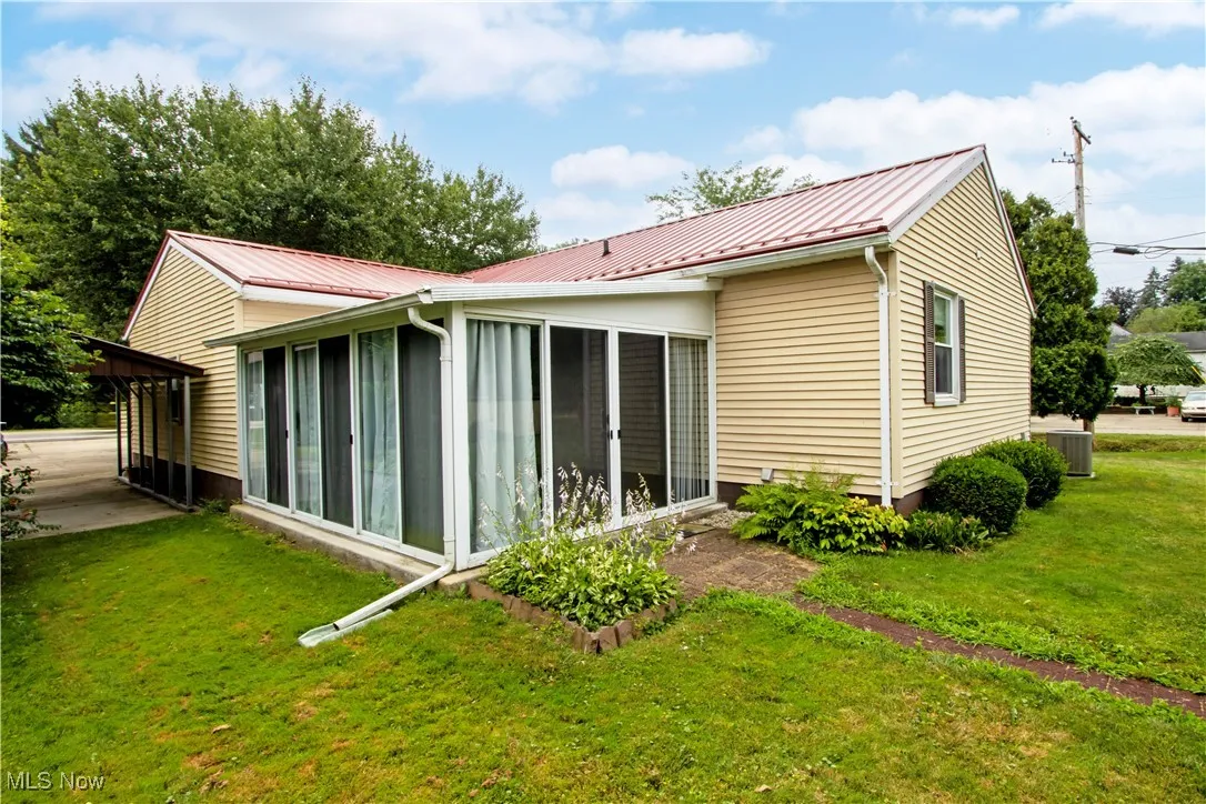 Rear view of property featuring a sunroom, a yard, and a metal roof