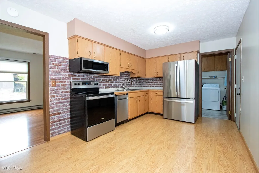 Kitchen featuring appliances with stainless steel finishes, washer / dryer, light wood-style floors, light brown cabinetry, and light countertops