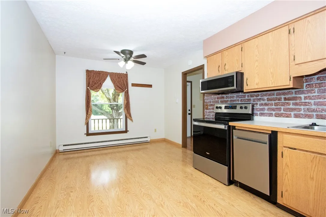Kitchen with stainless steel appliances, a baseboard radiator, light brown cabinets, light wood finished floors, and a textured ceiling