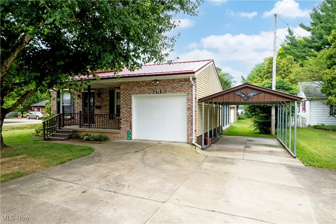 View of front of house with brick siding, a front lawn, a carport, driveway, and a metal roof
